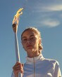 A female athlete solemnly carries the torch with flame on the opening Olympic ceremony against the blue sky