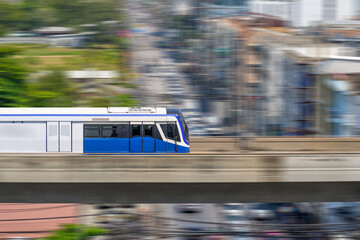 Poster - Speed modern commuter train, motion blur rides on a trestle bridge through buildings at height, side view