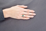 Fototapeta Tęcza - Beautiful female hand with gold ring with diamonds and emerald on gray background