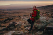 Young woman hiker with trekking poles resting against a rock, soft sunset light