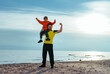 Happy boy and his father showing muscles on lake shore at summer, boy sitting on father's shoulder