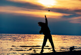 Fototapeta Sypialnia - Silhouette of boy throwing stone into the sea at sunset