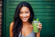 BlurredsSmiling young Asian woman holding a green smoothie and looking at camera