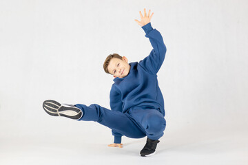 Boy in breakdancing position.Hip hop dance. Bboying basics. Boy in a blue tracksuit on a white background.Cheerful boy dancing breakdance