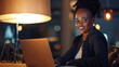 © Alina Tymofieieva - Portrait of a happy African American woman working on a laptop in the office. Young woman with laptop computer indoors at sunset.