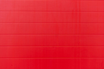 Close-up view of red painted wooden panel (or plastic siding) wall surface. Abstract red background. Copy space for your text or decoration. Construction industry and materials theme.