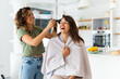 Cheerful young woman getting her hair done by female friend at home.