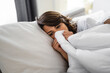 Young sick woman wrapped up in a blanket up to her nose lying in bed. Female person suffering from heat temperature, feeling cold and flu. Exhaustion due to illness.