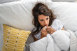 Young woman feeling sick and unwell while wrapped up in a blanket.