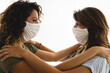 Closeup side view of young female adults looking face to face while wearing protective face mask. Support and care during illness.