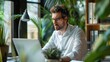 © Matthew - Focused individual working on a laptop surrounded by indoor plants, implying a green, productive work environment