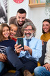 Vertical. Caucasian multi-generational family gathered at living room sitting on sofa using mobile phone. Happy people smiling with fun expression enjoying and watching videos together in cell at home