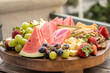 Round charcuterie board of mixed fruit with wedges of watermelon up in front next to grapes