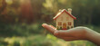 hand holding a small house outdoors with out of focus trees - real estate concept