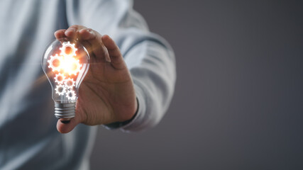 businessman Hand holding smart phone and light bulb with gear glowing with orange light and ray. Creative and new business knowledge thinking idea concept.	
