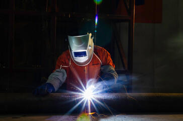 Handymen performing welding and grinding at their workplace in the workshop, while the sparks fly all around them, they wear a protective helmet and equipment.