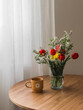 A spring bouquet of red tulips and spirea in a glass vase, a ceramic mug on a round wooden table