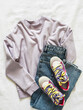 Fashionable teenage clothes - bright multicolored sneakers, lilac longsleeve and blue jeans on a light background, top view
