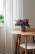 Living room interior - a bouquet of lilacs on a round wooden table and a Scandinavian-style chair