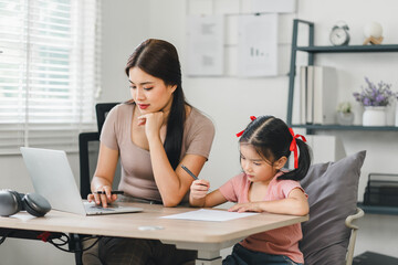 Wall Mural - Young mother working from home while assisting her daughter with homework during daytime