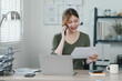 Smiling asian businesswoman talking on phone while reviewing document in bright office space.