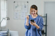 Excited woman celebrating good news on smartphone at home.