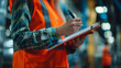 © khonkangrua - A male factory worker in an orange vest is focused on taking notes during a workplace inspection.