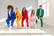 Funny cheerful group of young people dancers wearing bright colorful suits dancing together and having fun indoors. Full length portrait of happy friends at disco party enjoying good time together
