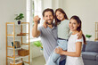 Happy joyful parents father, mother and their child girl holding house keys and looking cheerful at camera standing in new apartment. Family enjoying buying flat. Real estate and moving day concept.