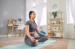 Beautiful relaxed young woman having yoga workout at home sitting on exercise mat in easy pose with closed eyes, doing meditation, taming stress, recharging before work week. Healthy lifestyle concept