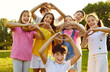 Portrait of a happy smiling children looking at the camera making heart shape gesture standing in the summer park outdoors. Thankful kids doing love sign by hands in nature in sunlight.