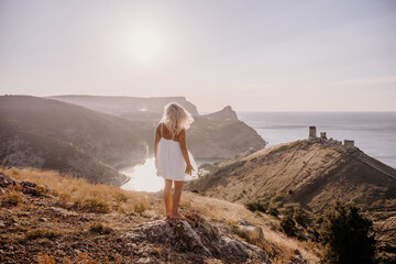 A woman stands on a hill overlooking a body of water. The sky is clear and the sun is shining brightly. The woman is enjoying the view and the peaceful atmosphere.