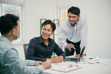 Poster - Three men are sitting at a table, one of them is pointing at a laptop