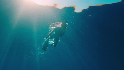 Canvas Print - Woman swims underwater in the tropical sea and slowly moves on the surface with sun shining through the water