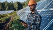 A man wearing a hard hat and holding a tablet stands in front of solar panels