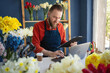 © Andrii Lysenko - Caucasian businessman in apron in small floral shop using laptop computer and clipboard for order details. Male florist at work. Own business