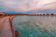 Perfect sunset on Maldives island, luxury water villas resort and wooden pier. Beautiful cloudy sky and beach background for summer vacation tourism travel vibes. Pristine sea water corals calm waves.