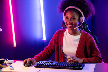 Wall Mural - African American girl streamer playing online fighting with Esport skilled team wearing headphones in neon color lighting room. Talking other players planing strategies to win competitors. Tastemaker.