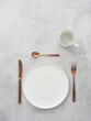 Table set with empty plate and cup, knife, fork and dessert spoon copper color on concrete background. Top view.