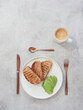 Top view of white plate with slices of toasted bread and sliced avocado in fan shape. Bronze colored coffee cup and silverware on gray table with copy space.