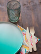 Utensils for eating outdoors or at a picnic on a wooden table. Empty green cardboard plate, glass, paper napkin and biodegradable cutlery, wooden fork and knife.