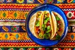 Two tacos on a blue plate on patterned tablecloth.