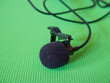 Lavalier Microphone Detail. A black lavalier microphone with foam windscreen and clip on a green background.