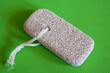 Skincare Tool Display. Pumice stone with string, presented on vibrant green, highlighting its exfoliating texture.