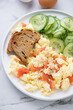 Scrambled eggs with smoked salmon, toasts and cucumber salad, vertical shot on a white marble background, middle close-up