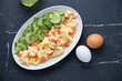 Scramble with smoked salmon and cucumber salad on a white plate, above view on a black marble background, horizontal shot