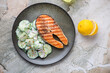 Olive-colored plate with cucumber salad and grilled salmon, flat lay on a light-beige granite background, horizontal shot