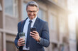 © peopleimages.com - City, coffee and phone with corporate man outdoor for morning commute to work in professional suit. App, social media and mature business person reading text message in urban town for communication