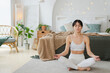 Yoga mindfulness meditation. Young healthy woman practicing yoga in living room at home. Woman sitting in lotus pose meditating smiling relaxing indoor. Girl doing breathing practice. Yoga at home