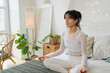 Yoga mindfulness meditation. Young healthy woman practicing yoga in bedroom at home. Woman sitting in lotus pose on bed meditating smiling relaxing indoor. Girl doing breathing practice. Yoga at home